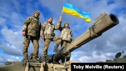 Украинские военнослужащие держат украинский флаг, позируя на танке Challenger 2 во время учений в лагере Бовингтон на юго-западе Великобритании. 22 февраля 2023 года